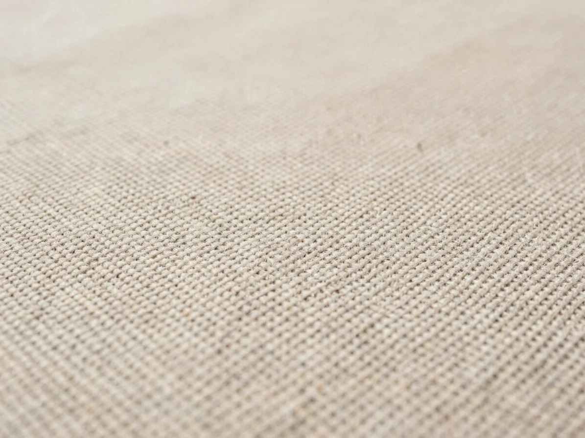 Tactile close-up of natural-fiber textile fabric surface with visible weave structure, soft diffused daylight, unbleache